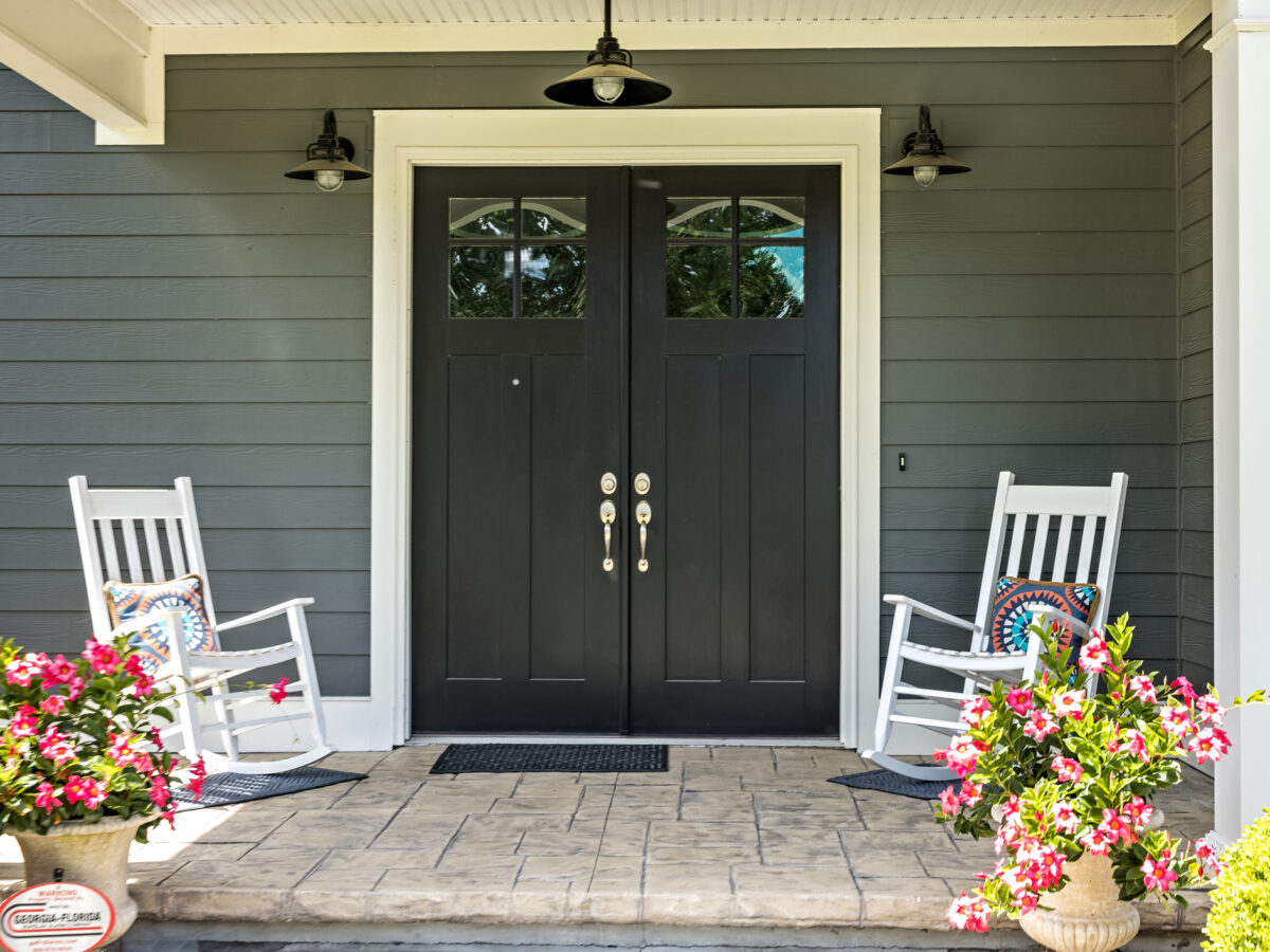 A front porch with two rocking chairs, stamped concrete floors, and double glass doors.