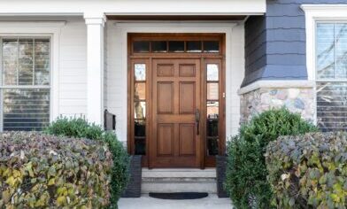 A wooden front door, surrounded by windows, with white, blue, and stone siding.