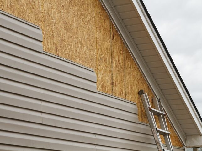 New beige vinyl siding being installed over an osb (oriented strand board) substrate on a residential house in the Southeastern USA region on a cloudy day. The old vinyl siding was being replaced after a hail storm.